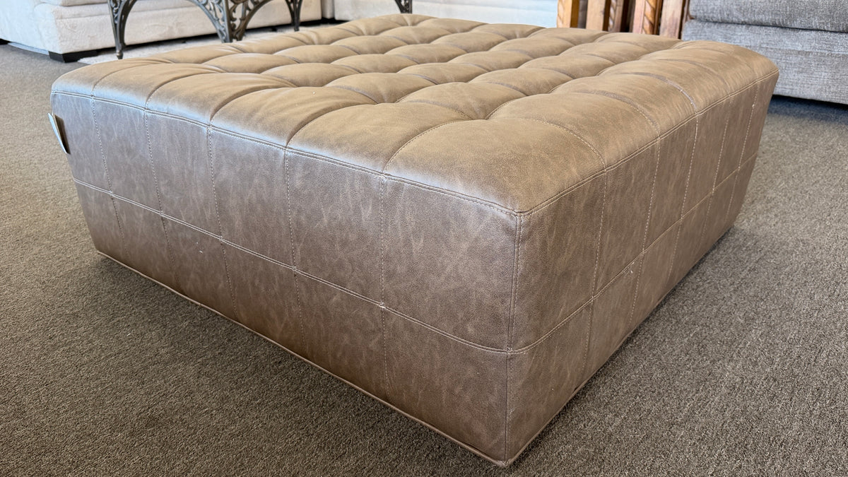 A large square tufted ottoman upholstered in distressed taupe and mushroom faux leather in excellent condition.