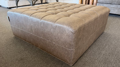 A large square tufted ottoman upholstered in distressed taupe and mushroom faux leather in excellent condition.