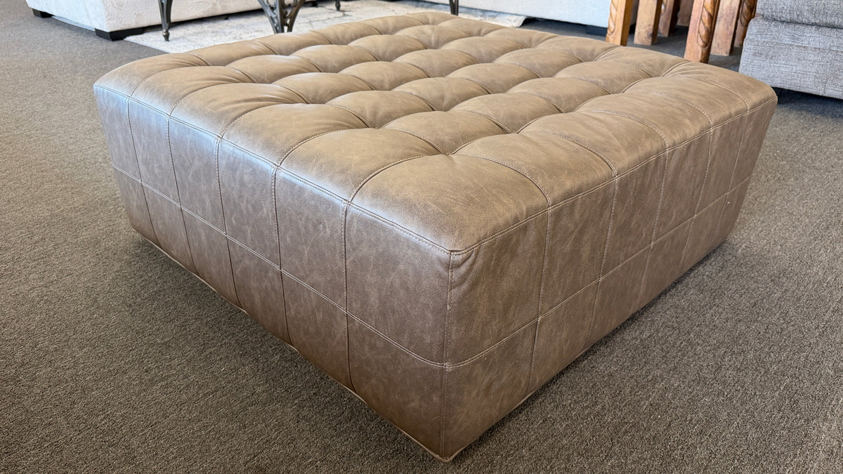 A large square tufted ottoman upholstered in distressed taupe and mushroom faux leather in excellent condition.
