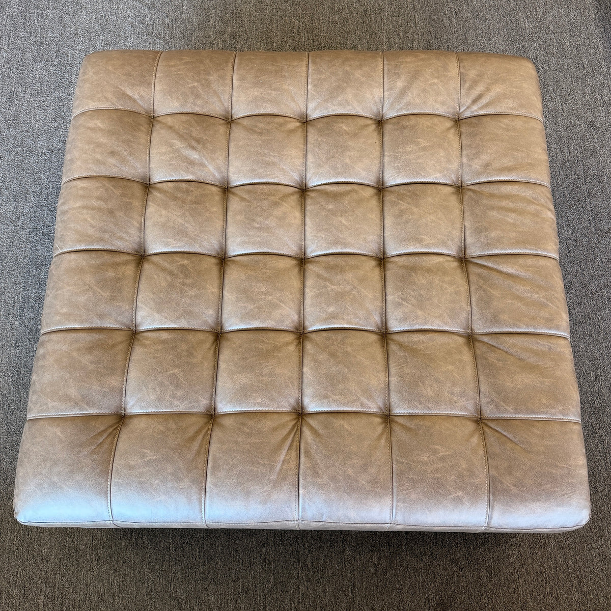 A large square tufted ottoman upholstered in distressed taupe and mushroom faux leather in excellent condition.