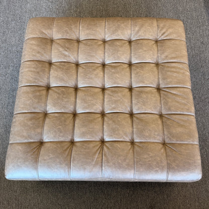 A large square tufted ottoman upholstered in distressed taupe and mushroom faux leather in excellent condition.