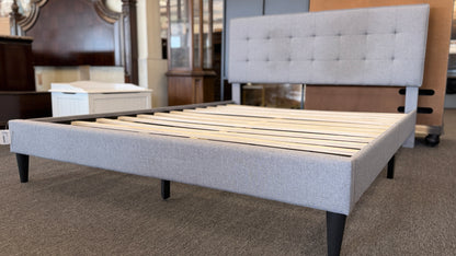 Light gray upholstered queen platform bed featuring a button-tufted headboard, matching upholstered side rails, dark tapered wooden legs, and wooden slat mattress support.