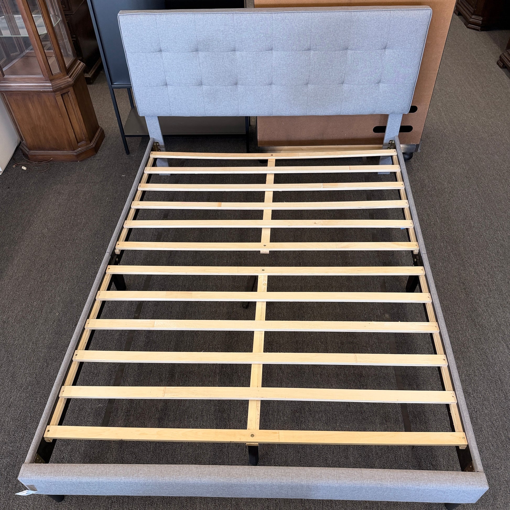 Light gray upholstered queen platform bed featuring a button-tufted headboard, matching upholstered side rails, dark tapered wooden legs, and wooden slat mattress support.