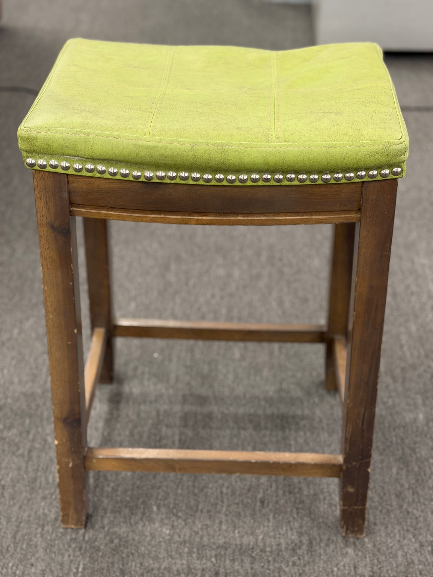 A wooden backless barstool featuring a lime green cushioned leather seat with brass nailhead accents in good condition.