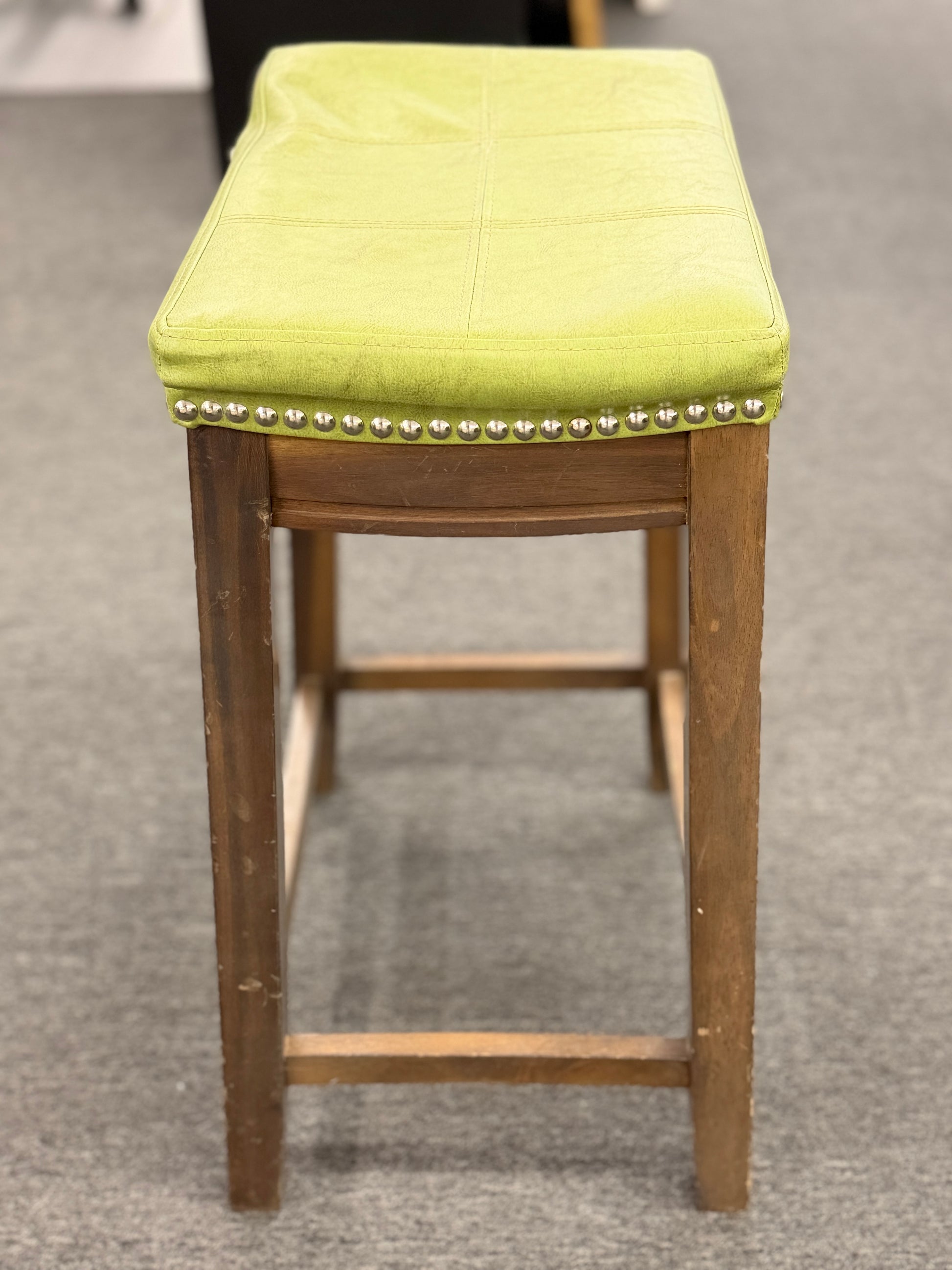 A wooden backless barstool featuring a lime green cushioned leather seat with brass nailhead accents in good condition.