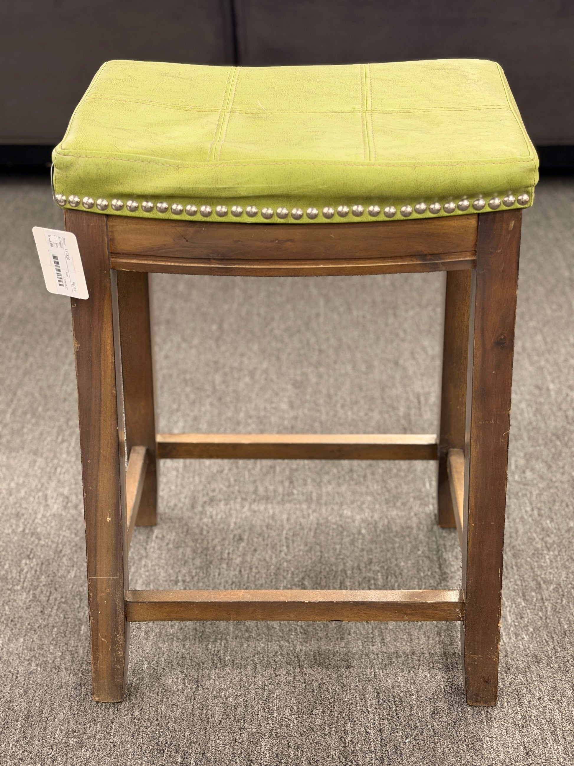 A wooden backless barstool featuring a lime green cushioned leather seat with brass nailhead accents in good condition.
