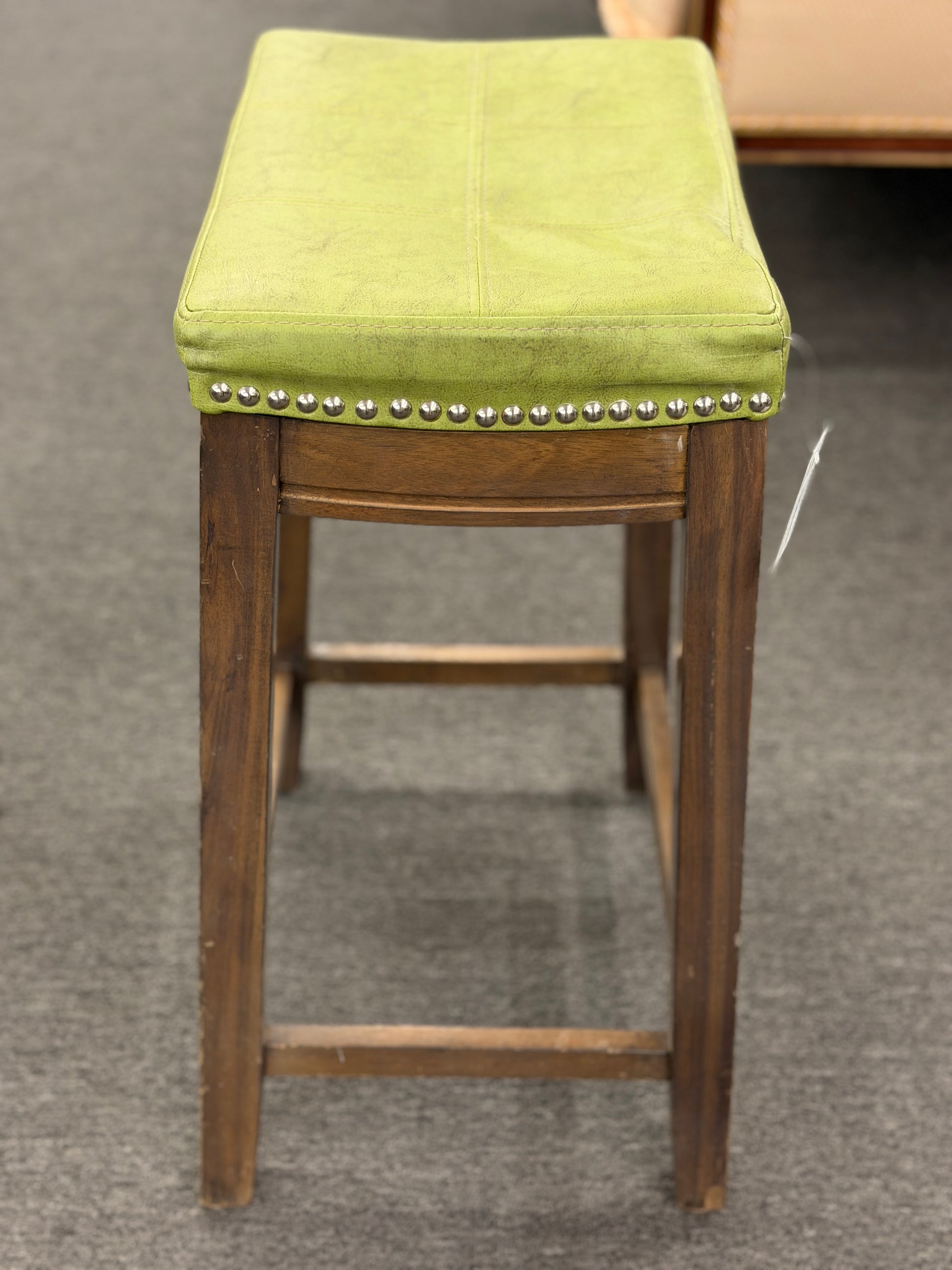 A wooden backless barstool featuring a lime green cushioned leather seat with brass nailhead accents in good condition.