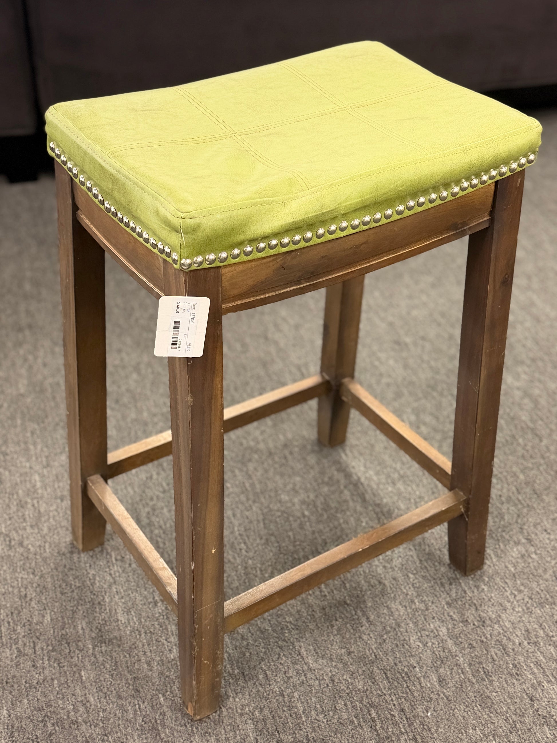 A wooden backless barstool featuring a lime green cushioned leather seat with brass nailhead accents in good condition.