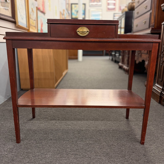 A classic mahogany-finished wooden console entry table featuring a center drawer with oval brass pull, tapered legs, and a lower shelf.