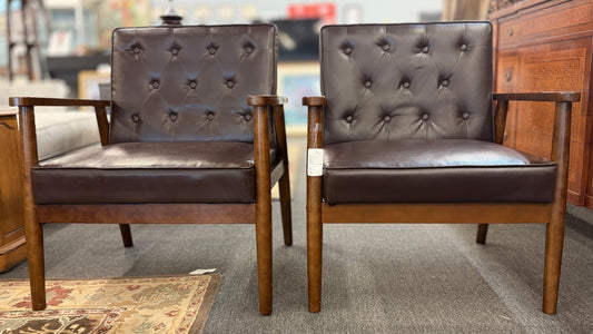 A pair of mid-century modern style accent armchairs featuring dark brown button-tufted backrests, smooth seat cushions, and exposed medium-toned wooden frames with tapered legs.