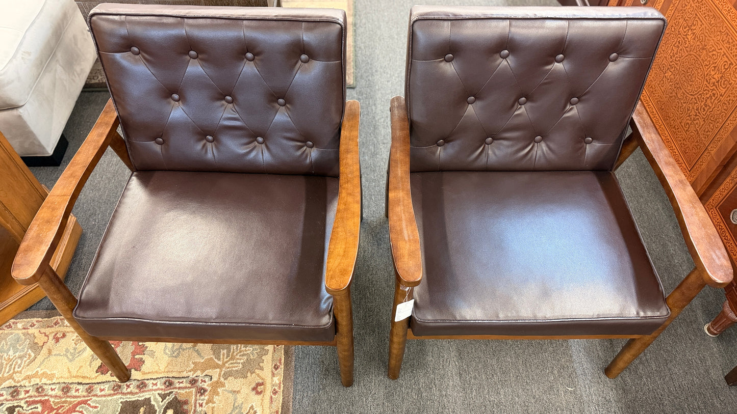 A pair of mid-century modern style accent armchairs featuring dark brown button-tufted backrests, smooth seat cushions, and exposed medium-toned wooden frames with tapered legs.