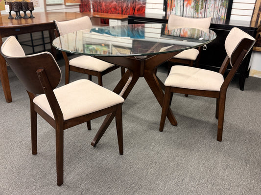 A mid-century modern dining set consisting of a round glass-top table on an angled dark-wood base paired with four curved-back off-white upholstered chairs in good condition.