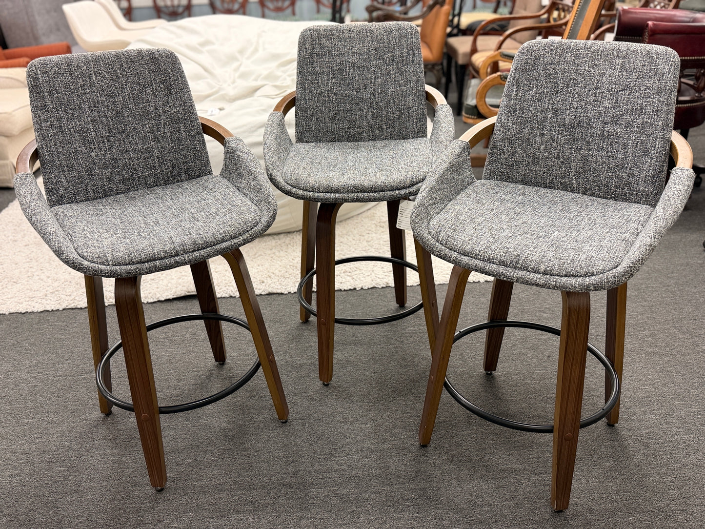 A 3-piece set of mid-century modern barstools featuring textured gray tweed upholstered seats, curved walnut wood armrests, and tapered legs with a black metal footrest ring.