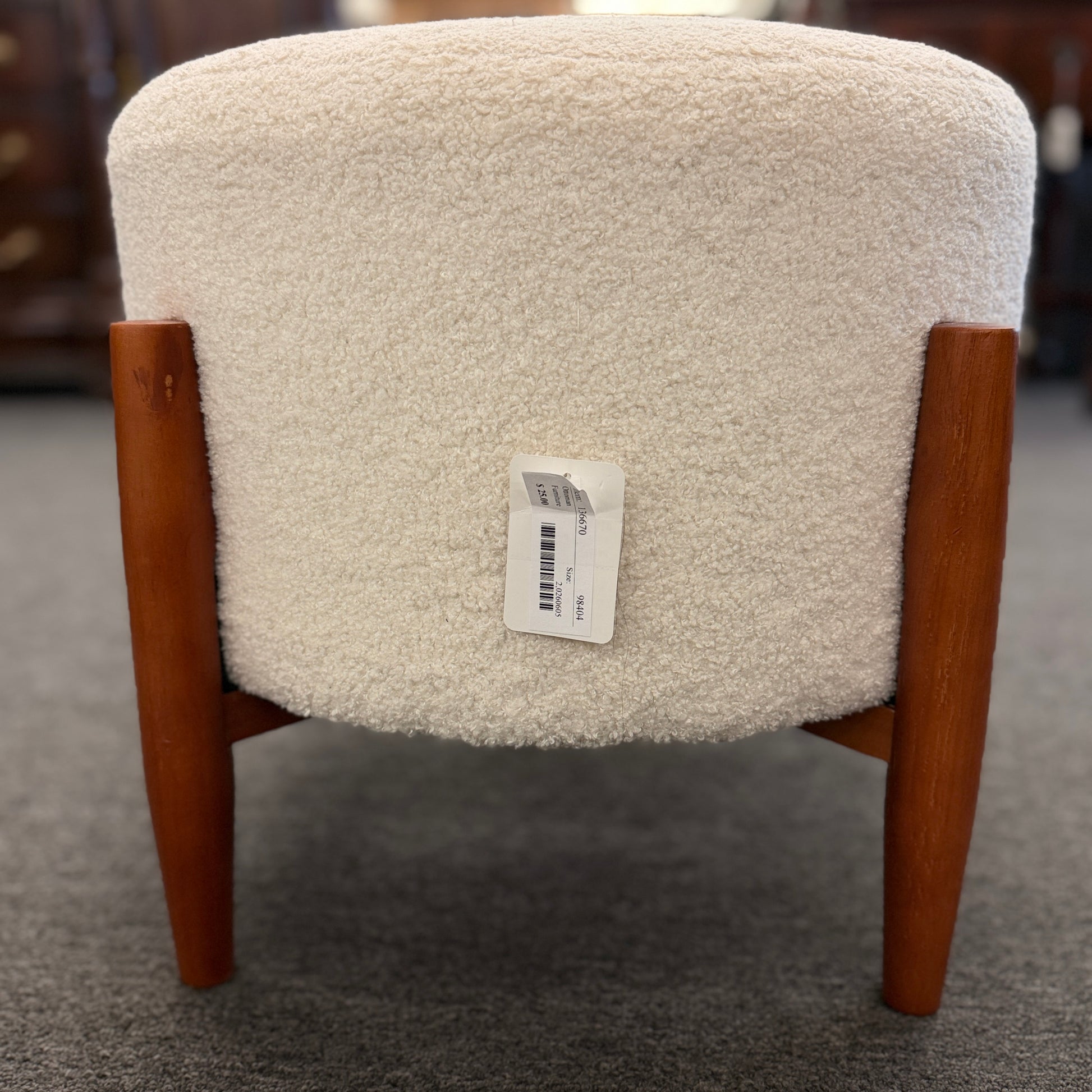 A mid-century modern round accent ottoman featuring a plush, fabric-upholstered cylindrical seat on a structured, four-legged exposed wooden base.