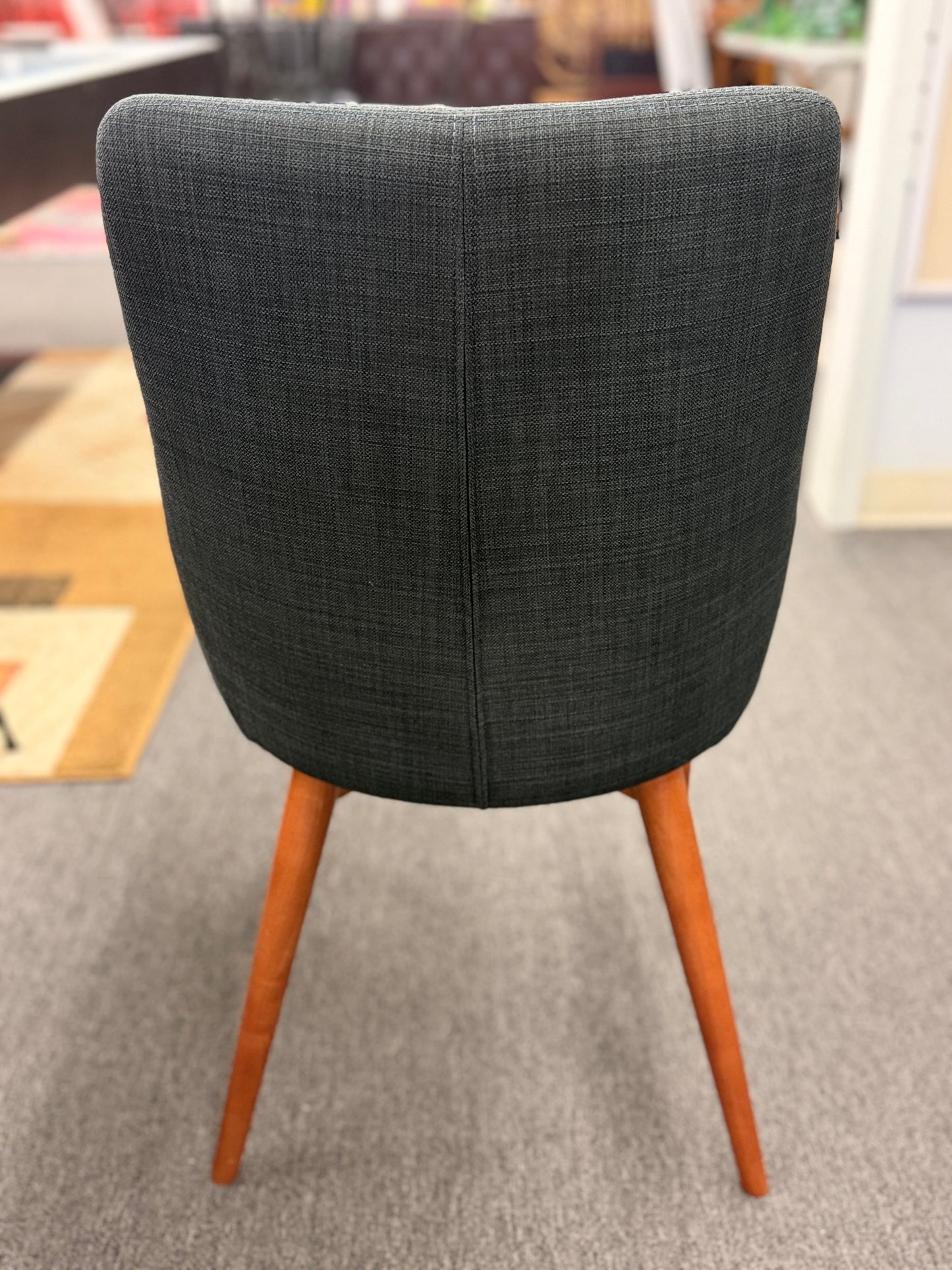 A mid-century modern dining set featuring a round white tabletop with tapered wooden legs and four dark gray upholstered chairs.