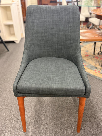 A mid-century modern dining set featuring a round white tabletop with tapered wooden legs and four dark gray upholstered chairs.