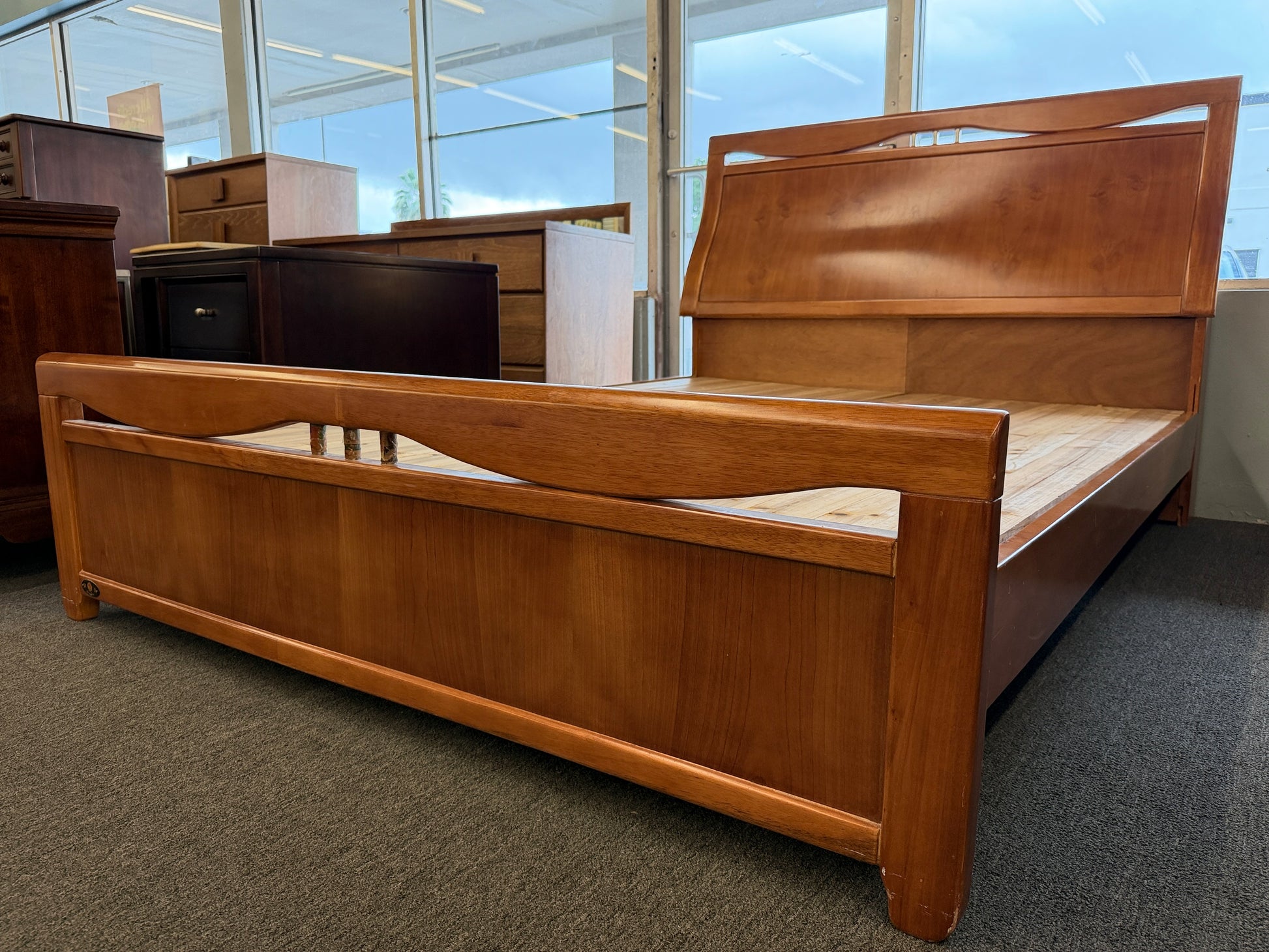 A mid-century modern full bed frame made of wood, featuring a gently curved headboard, footboard, and a sturdy interior slatted support base.