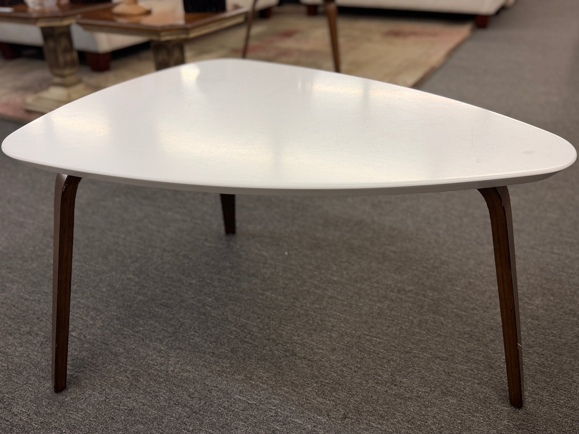 A retro-inspired triangular end table featuring a smooth white guitar-pick-shaped top supported by three splayed, tapered dark wood legs.