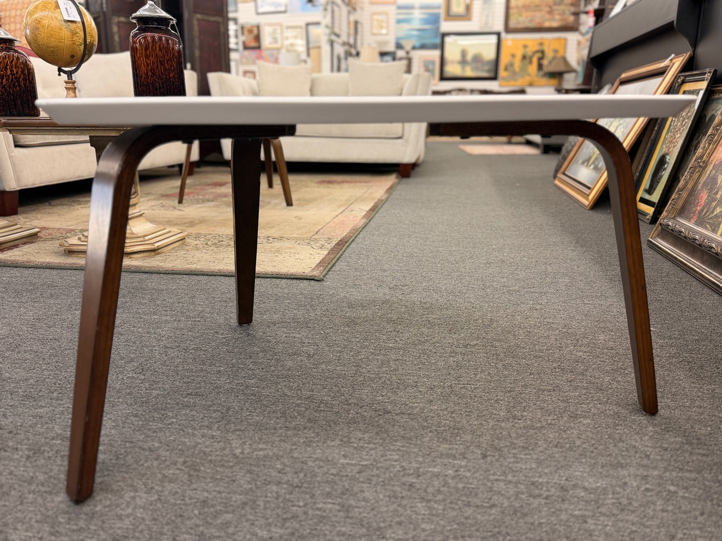 A retro-inspired triangular end table featuring a smooth white guitar-pick-shaped top supported by three splayed, tapered dark wood legs.