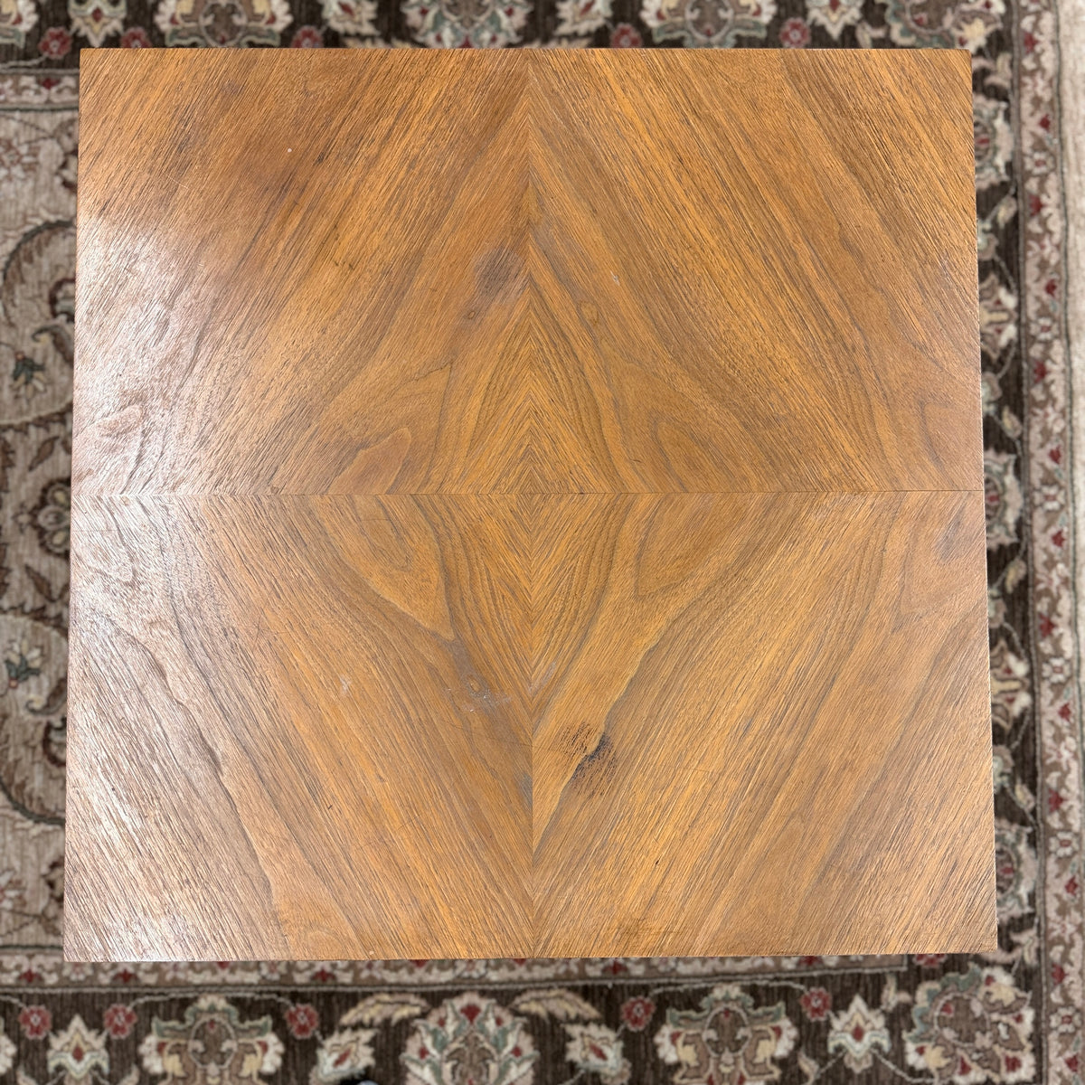 A mid-century inspired square wooden coffee table featuring a parquet veneer top, single drawer with antique brass pulls, and a central pedestal on a flat plinth base in good condition.