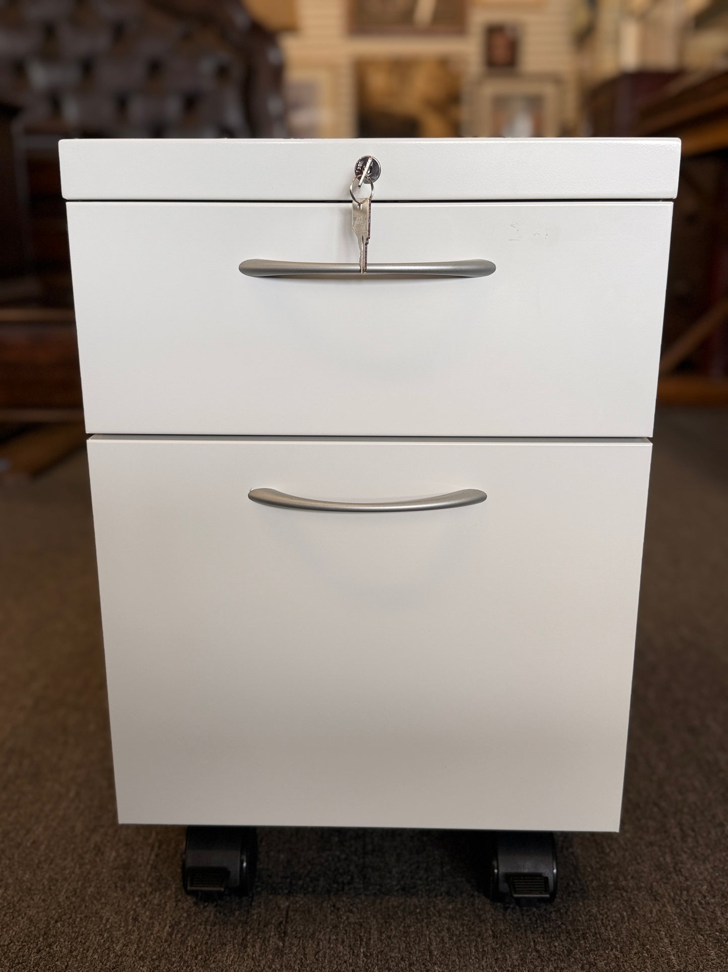 A minimalist two-drawer under-desk pedestal file cabinet featuring curved metal handles, a top lock, and dual casters in good condition.