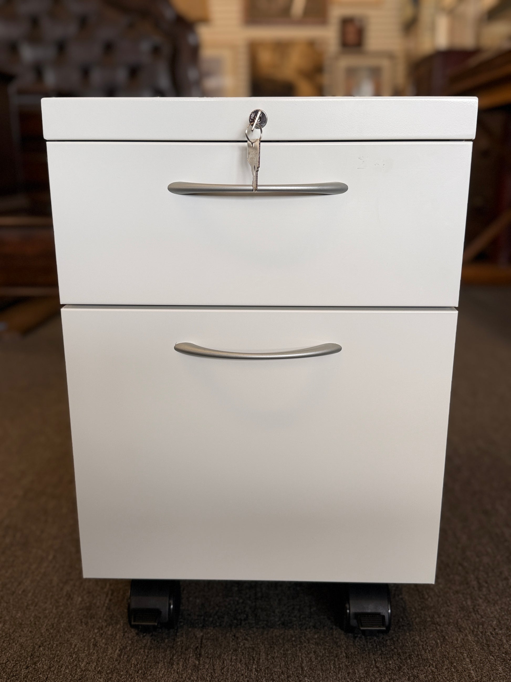 A minimalist two-drawer under-desk pedestal file cabinet featuring curved metal handles, a top lock, and dual casters in good condition.