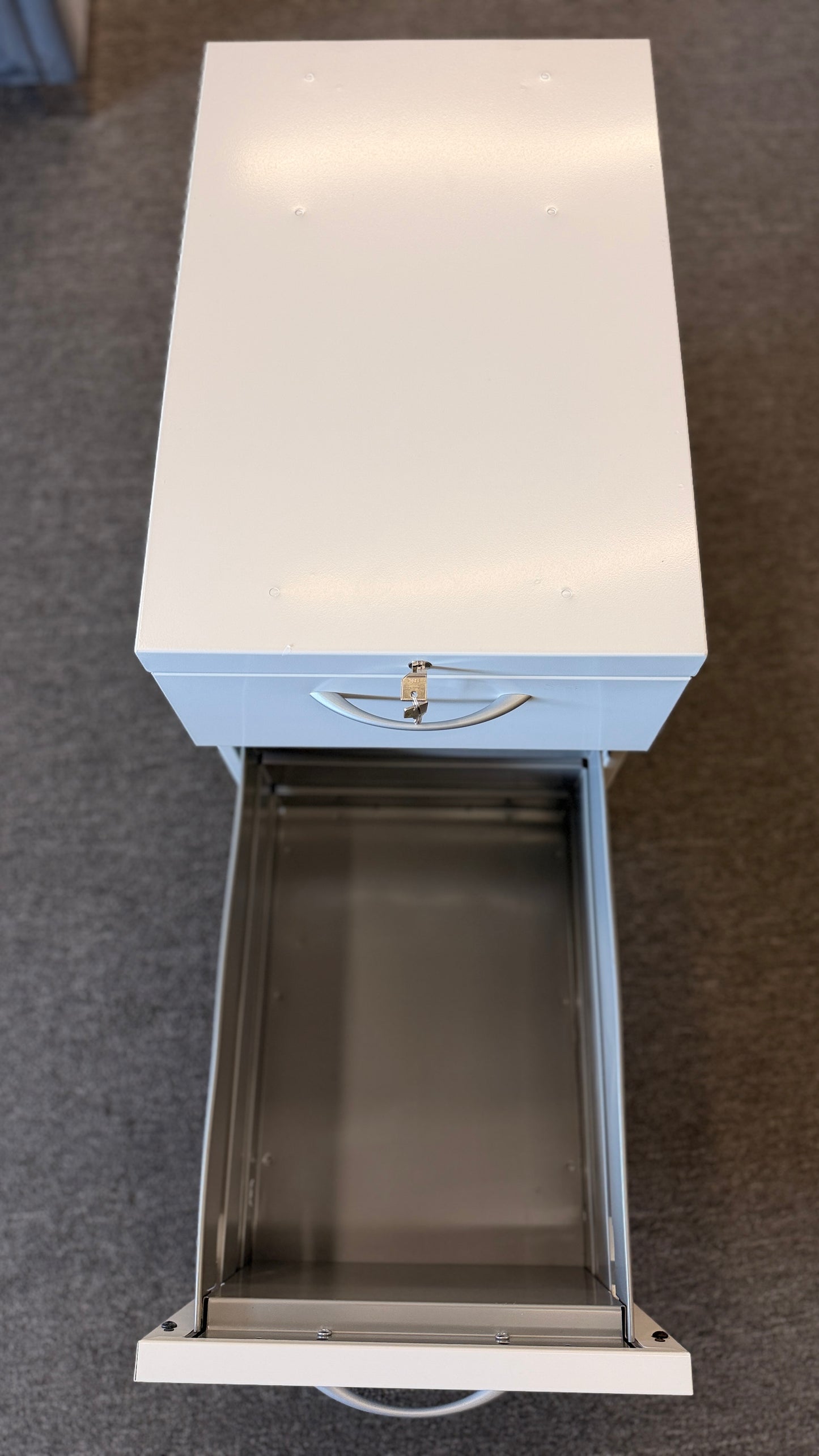 A minimalist two-drawer under-desk pedestal file cabinet featuring curved metal handles, a top lock, and dual casters in good condition.