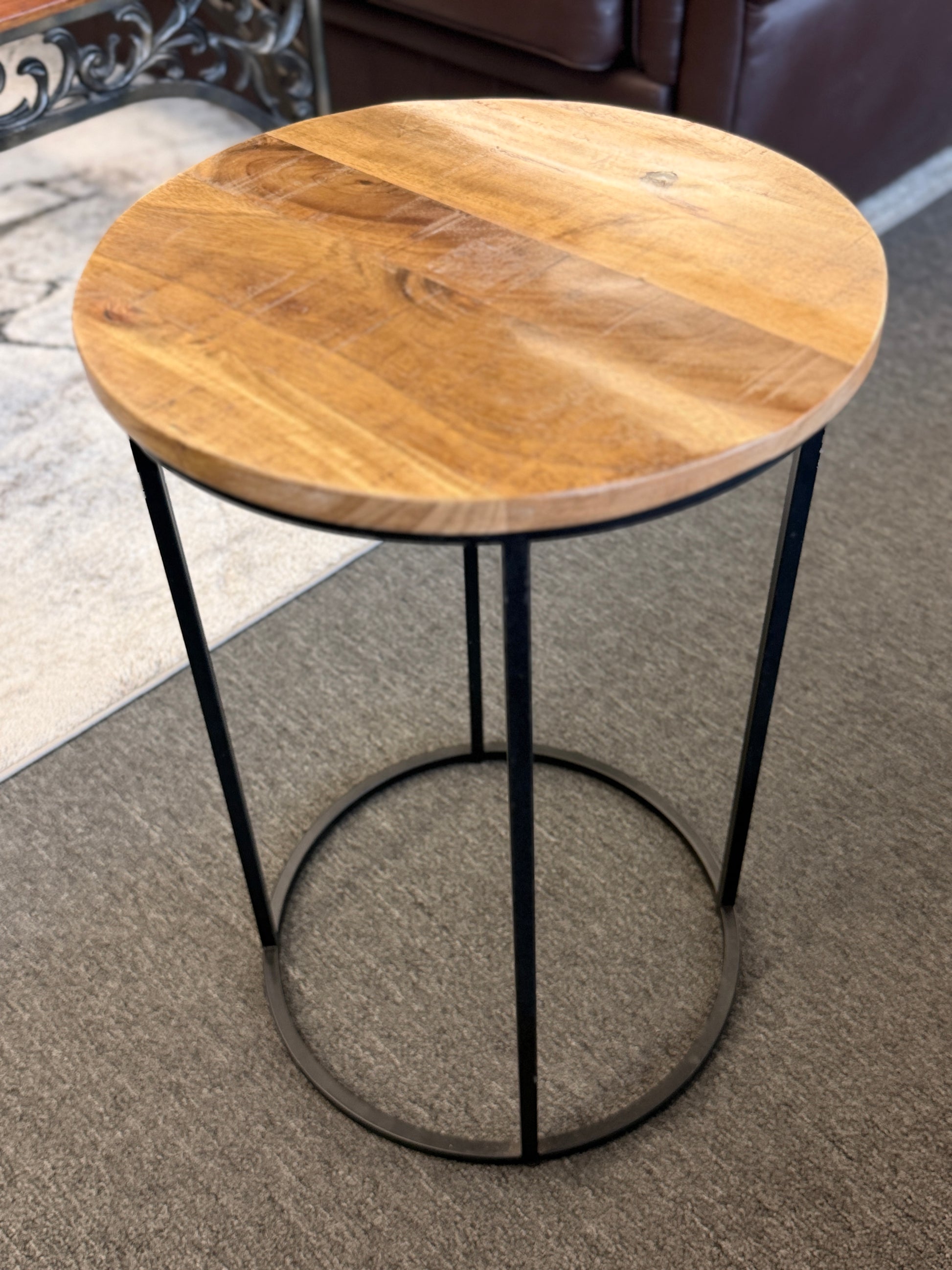 A minimalist round side table featuring a light wood tabletop and a black metal frame in excellent condition.