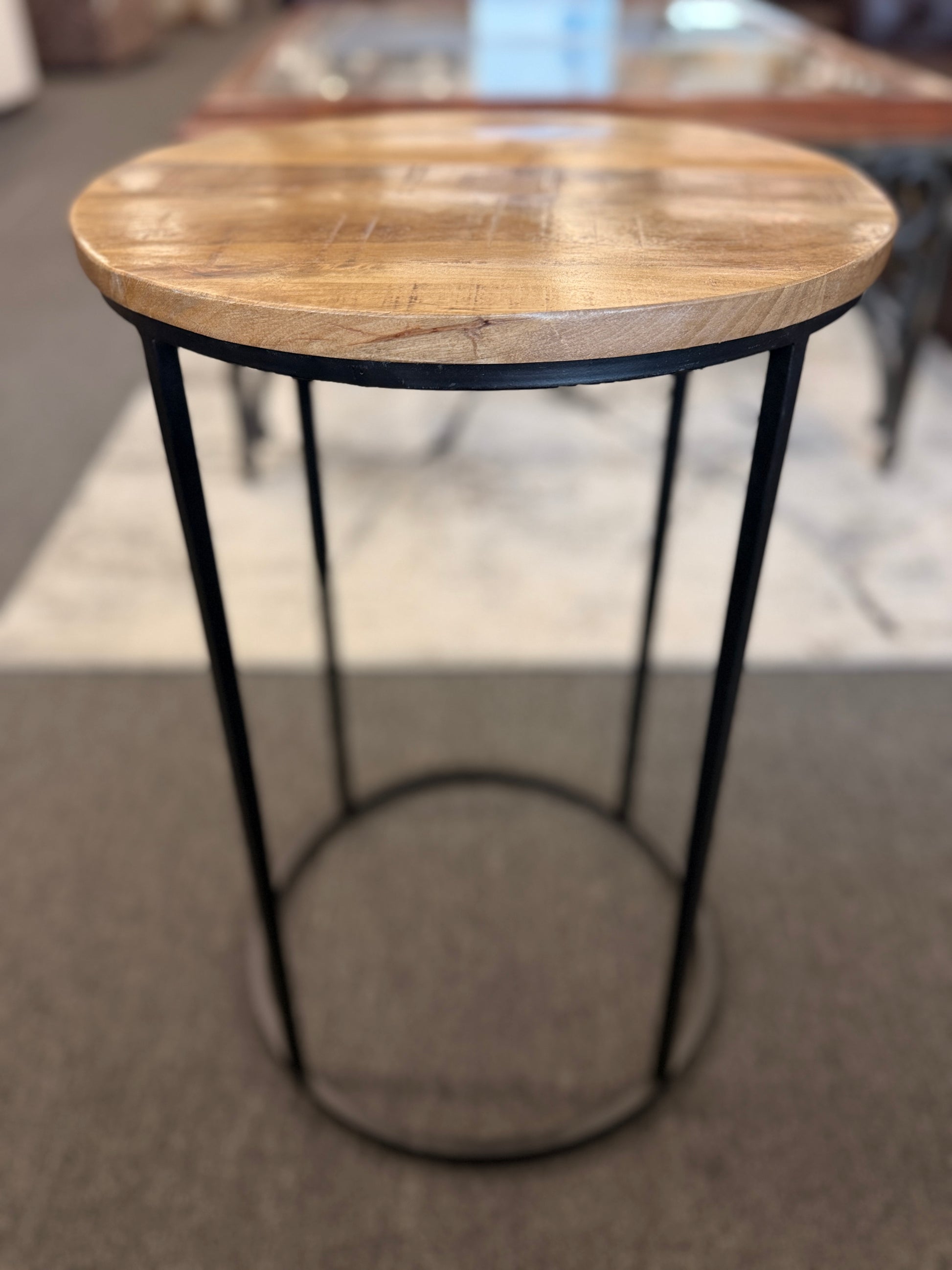 A minimalist round side table featuring a light wood tabletop and a black metal frame in excellent condition.