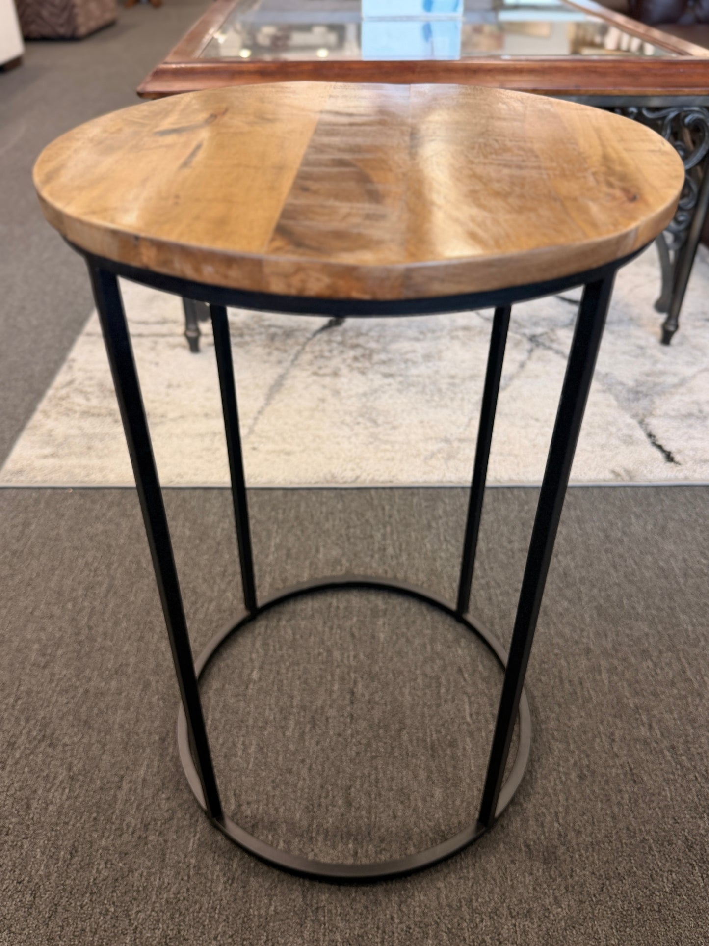 A minimalist round side table featuring a light wood tabletop and a black metal frame in excellent condition.