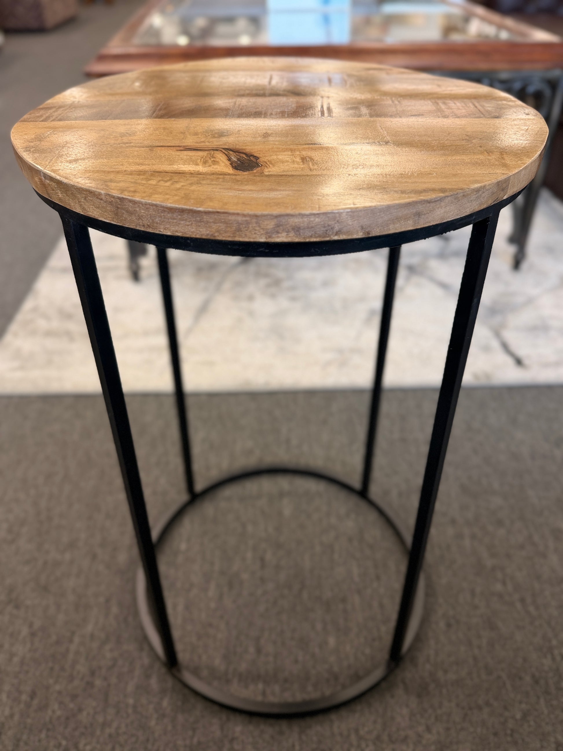 A minimalist round side table featuring a light wood tabletop and a black metal frame in excellent condition.
