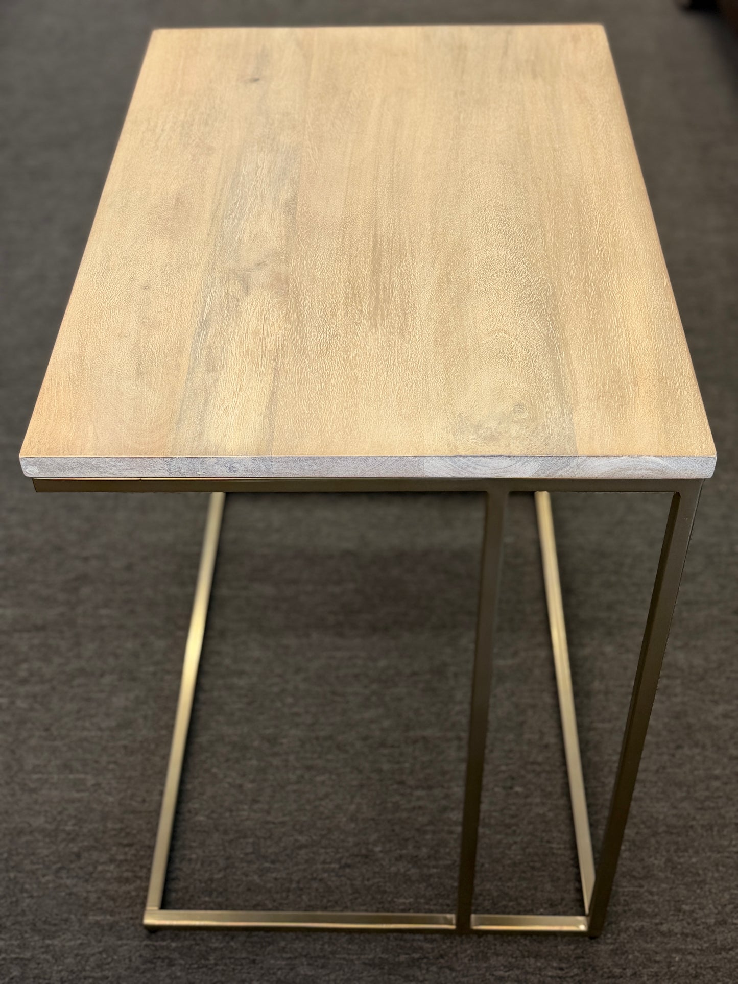A minimalist C-shaped end table with a wooden tabletop and a slender black metal frame designed to slide over a sofa arm.