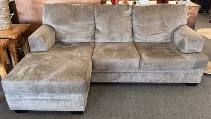 A modern casual sectional sofa upholstered in textured beige-gray chenille fabric featuring an extended chaise lounge in excellent condition.