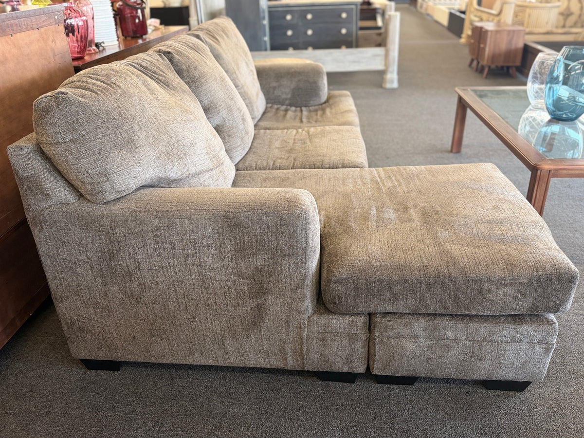 A modern casual sectional sofa upholstered in textured beige-gray chenille fabric featuring an extended chaise lounge in excellent condition.