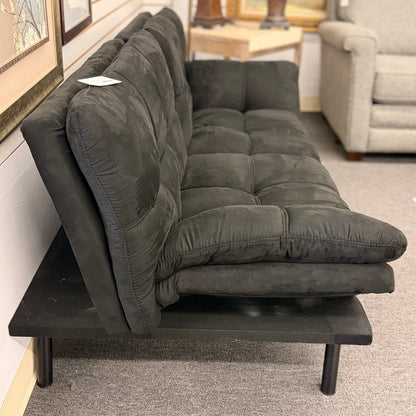 A modern dark charcoal tufted futon sofa featuring adjustable fold-down backrests, pillow-style armrests, and tapered black metal legs.