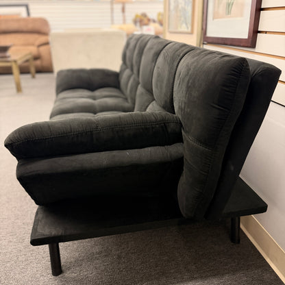 A modern dark charcoal tufted futon sofa featuring adjustable fold-down backrests, pillow-style armrests, and tapered black metal legs.