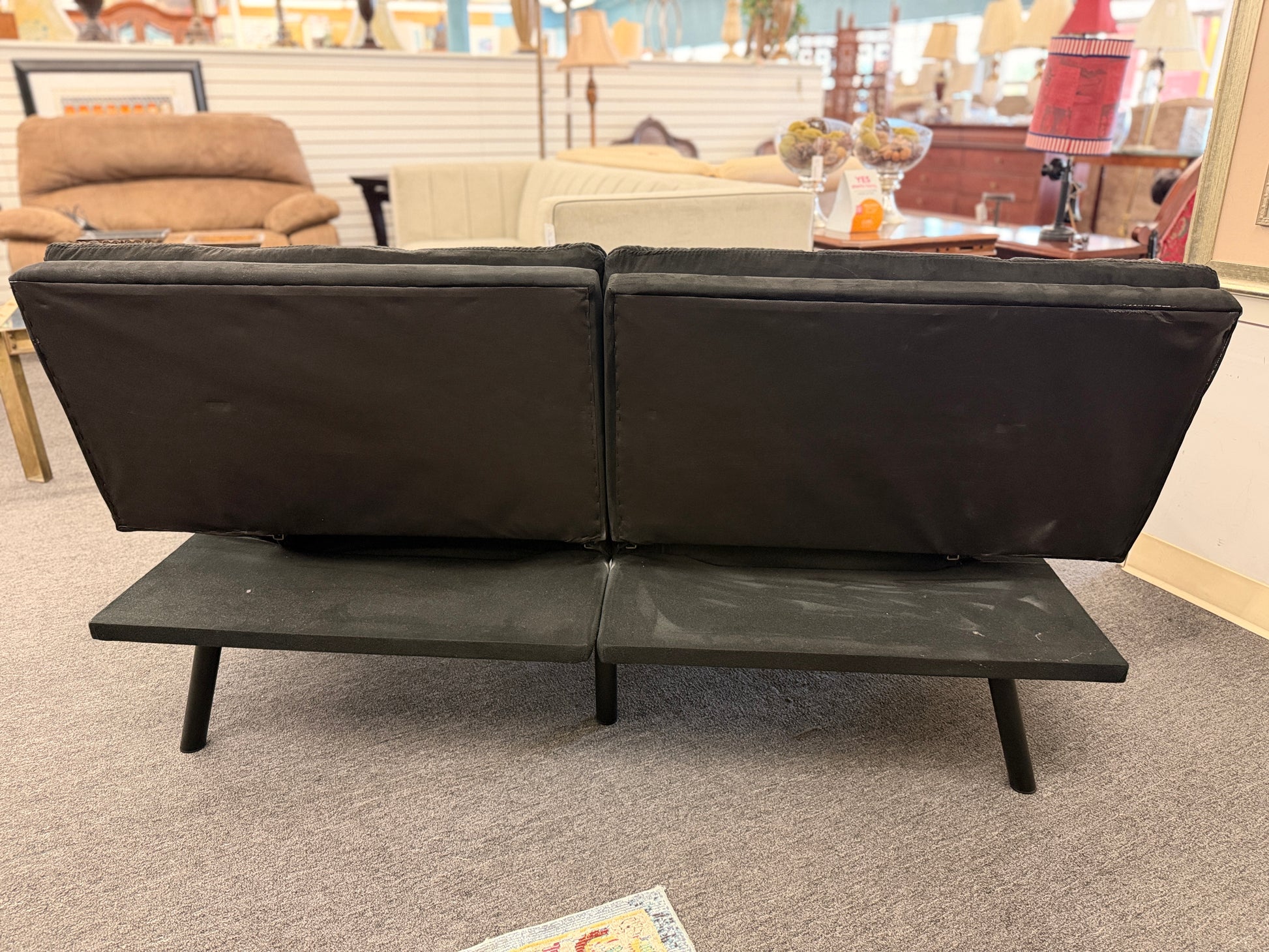 A modern dark charcoal tufted futon sofa featuring adjustable fold-down backrests, pillow-style armrests, and tapered black metal legs.