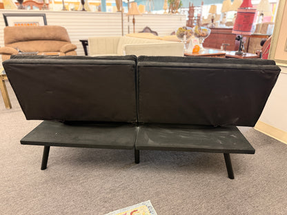 A modern dark charcoal tufted futon sofa featuring adjustable fold-down backrests, pillow-style armrests, and tapered black metal legs.