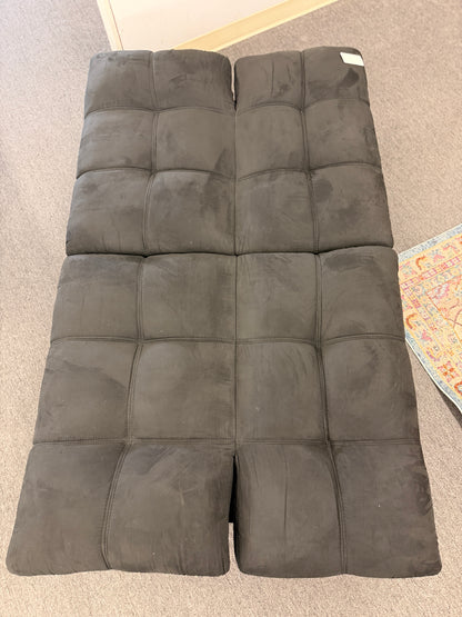 A modern dark charcoal tufted futon sofa featuring adjustable fold-down backrests, pillow-style armrests, and tapered black metal legs.