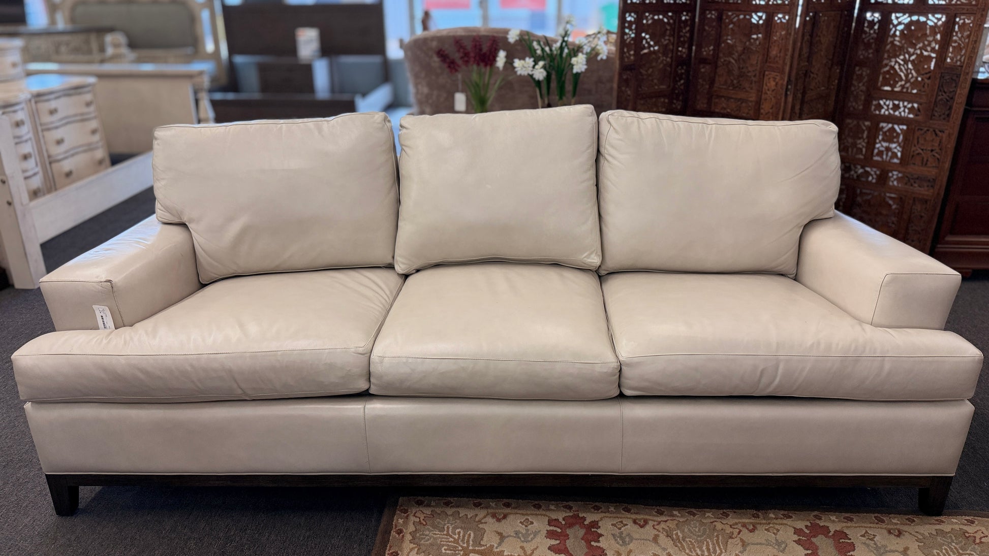 A modern deep-seated three-cushion leather sofa featuring structured track arms, loose back pillows, and an exposed dark wood base in good condition.