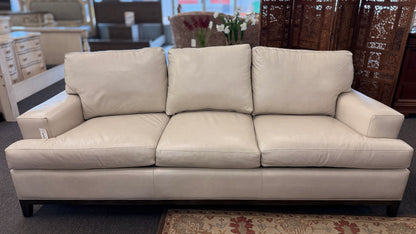 A modern deep-seated three-cushion leather sofa featuring structured track arms, loose back pillows, and an exposed dark wood base in good condition.