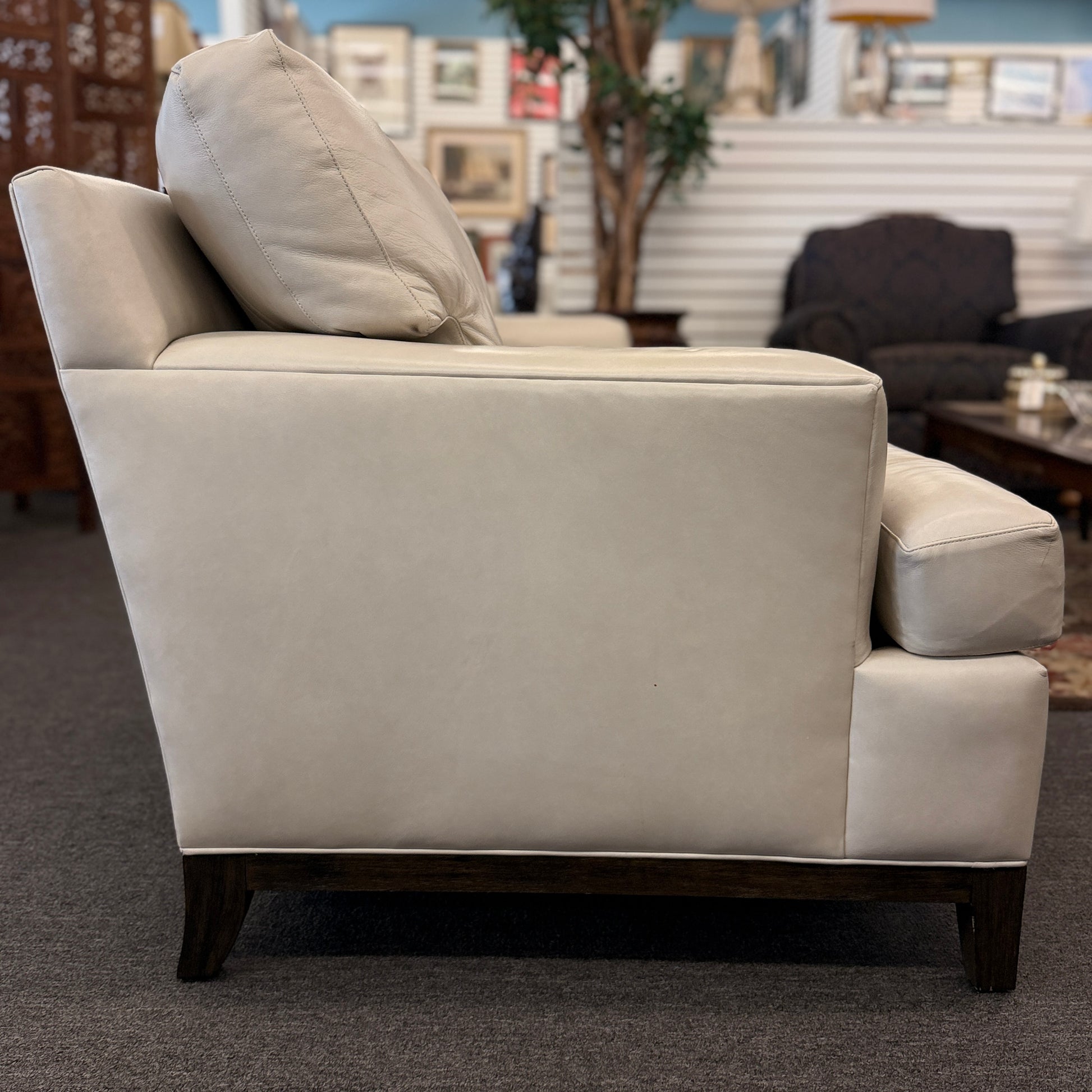 A modern deep-seated three-cushion leather sofa featuring structured track arms, loose back pillows, and an exposed dark wood base in good condition.