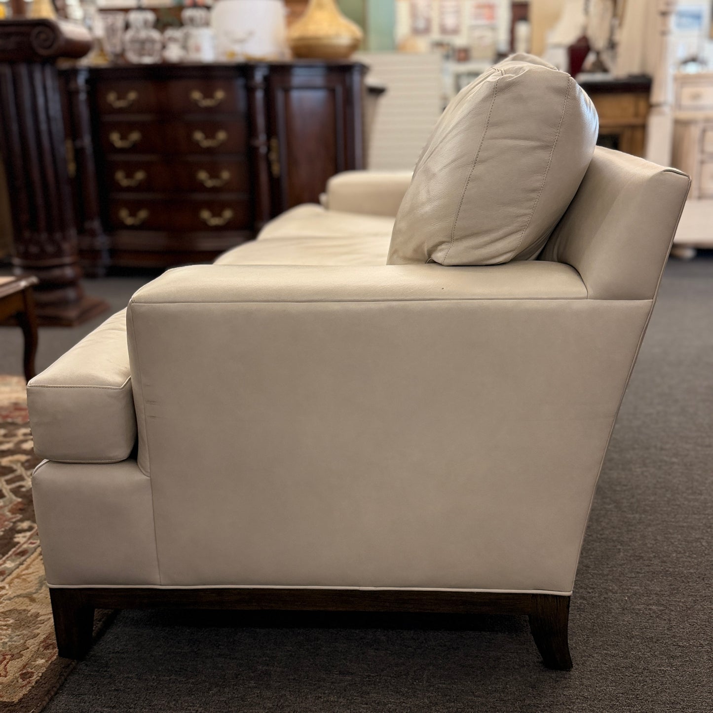 A modern deep-seated three-cushion leather sofa featuring structured track arms, loose back pillows, and an exposed dark wood base in good condition.