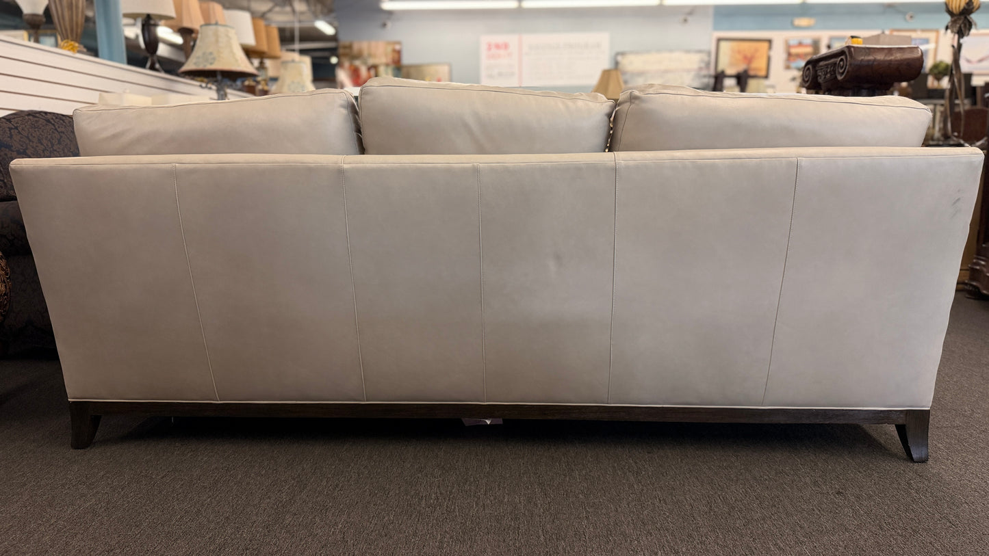 A modern deep-seated three-cushion leather sofa featuring structured track arms, loose back pillows, and an exposed dark wood base in good condition.