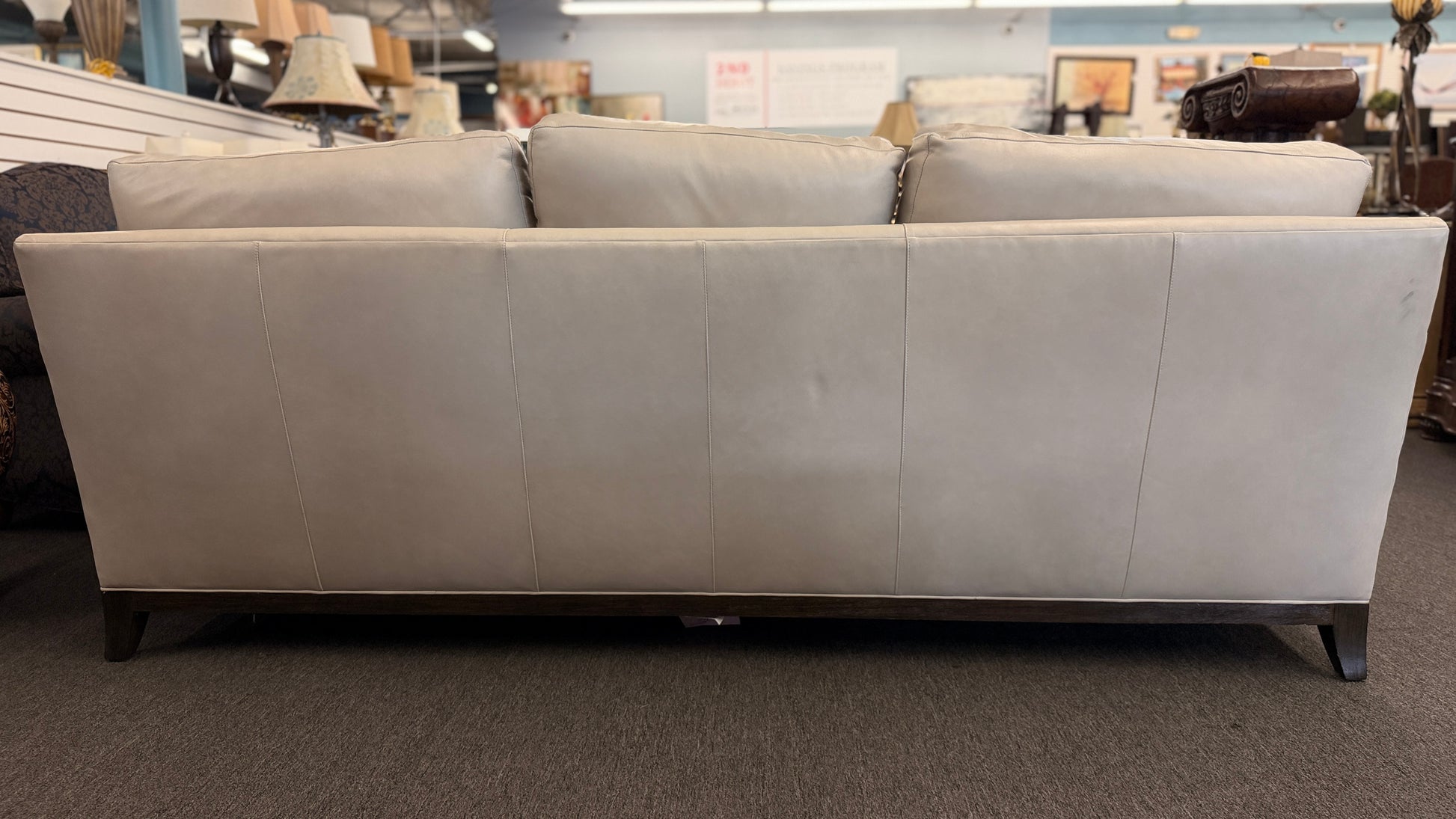 A modern deep-seated three-cushion leather sofa featuring structured track arms, loose back pillows, and an exposed dark wood base in good condition.