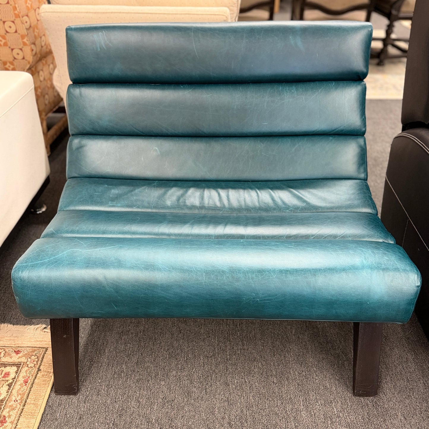 Modern armless accent chair upholstered in distressed teal leather featuring horizontal channel tufting and dark square wooden legs.