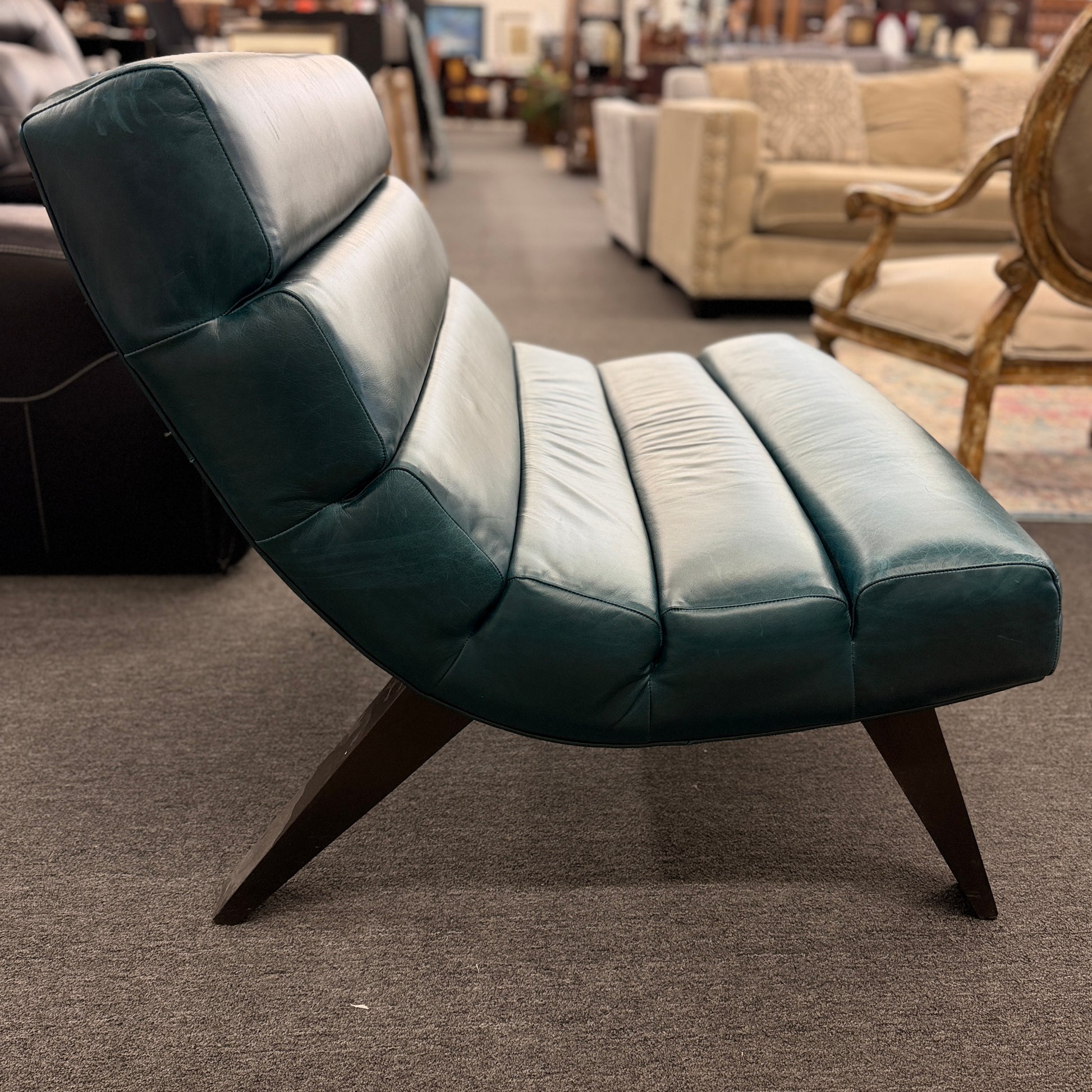 Modern armless accent chair upholstered in distressed teal leather featuring horizontal channel tufting and dark square wooden legs.