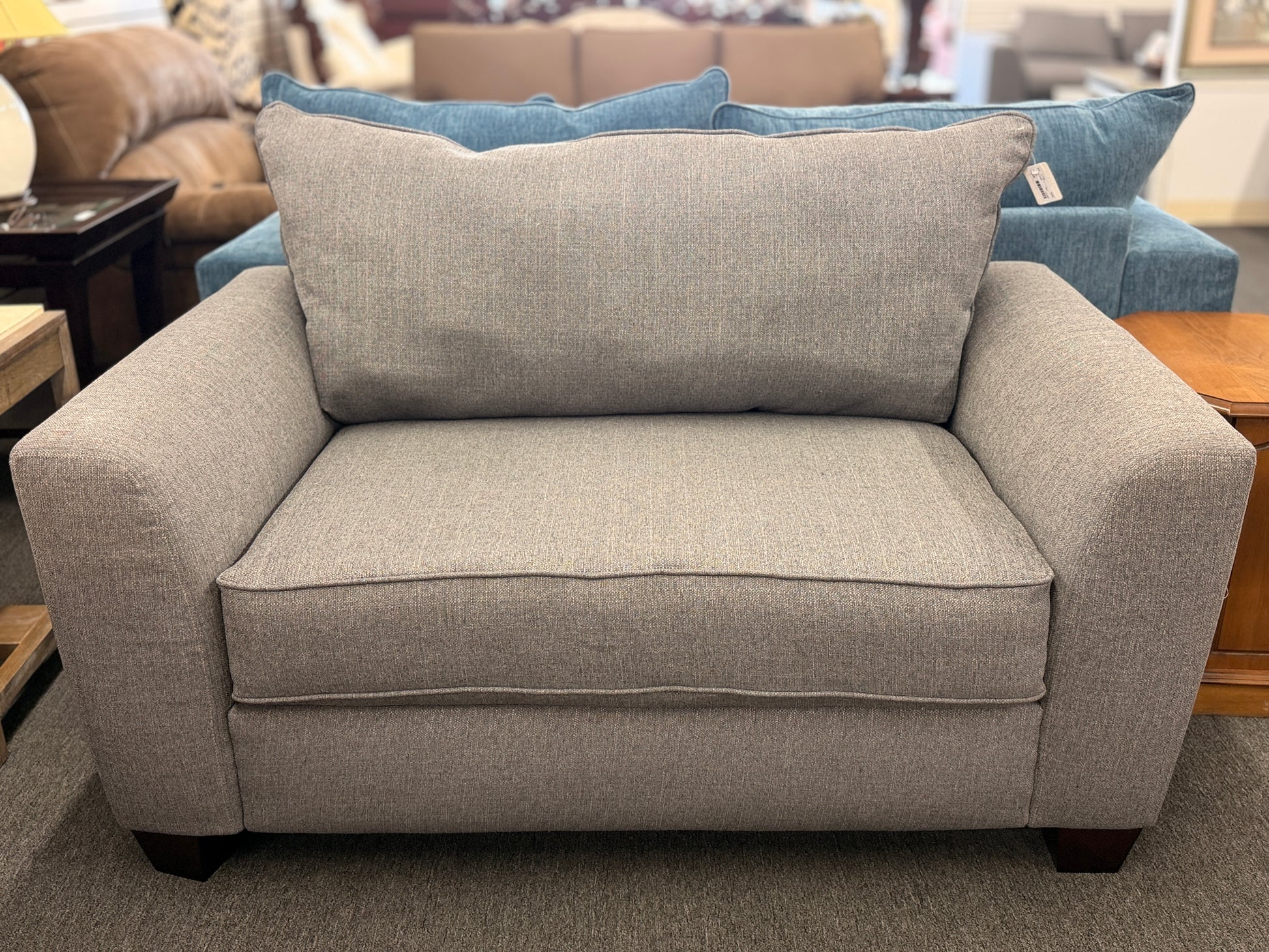 An oversized chair-and-a-half sleeper loveseat upholstered in neutral textured grey-beige fabric featuring wide track arms and plush cushioning.