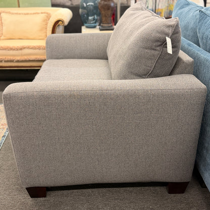 An oversized chair-and-a-half sleeper loveseat upholstered in neutral textured grey-beige fabric featuring wide track arms and plush cushioning.