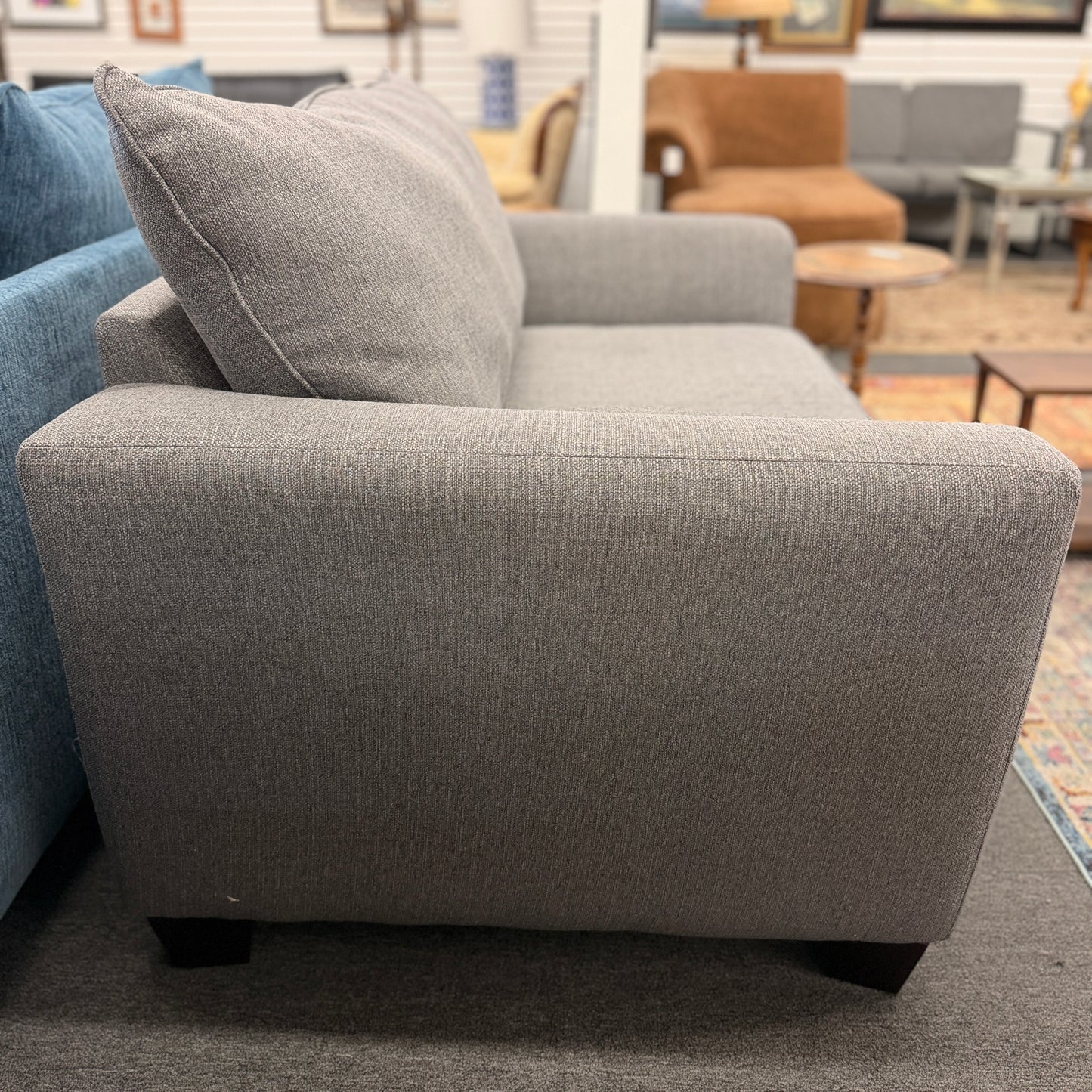 An oversized chair-and-a-half sleeper loveseat upholstered in neutral textured grey-beige fabric featuring wide track arms and plush cushioning.
